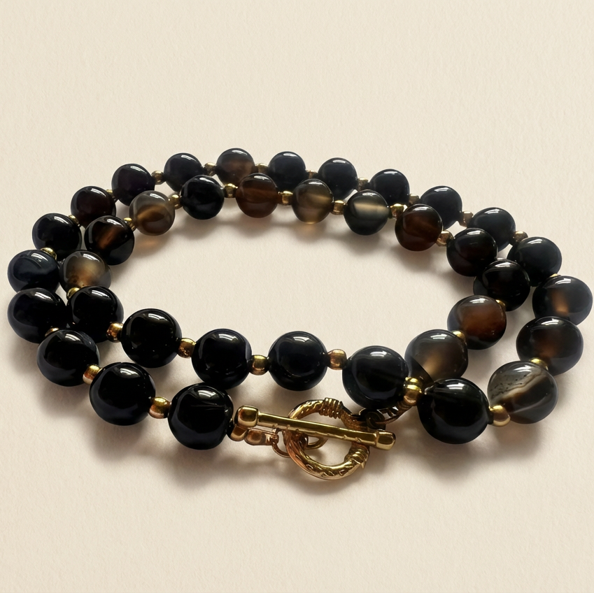 Black beaded bracelet with a gold clasp on a beige background