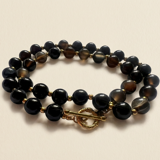 Black beaded bracelet with a gold clasp on a beige background