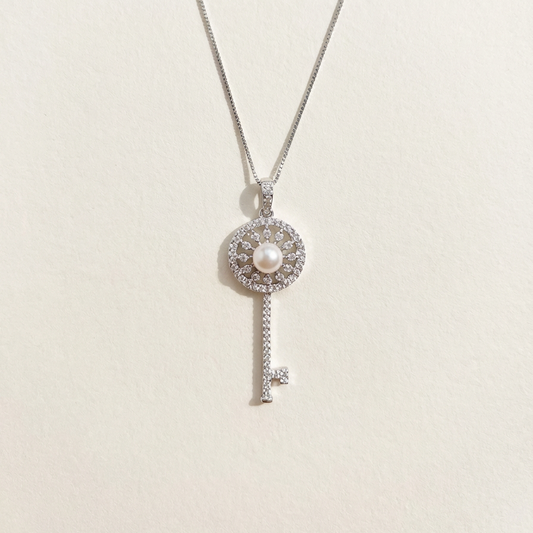 Silver key-shaped pendant necklace with a pearl on a light beige background