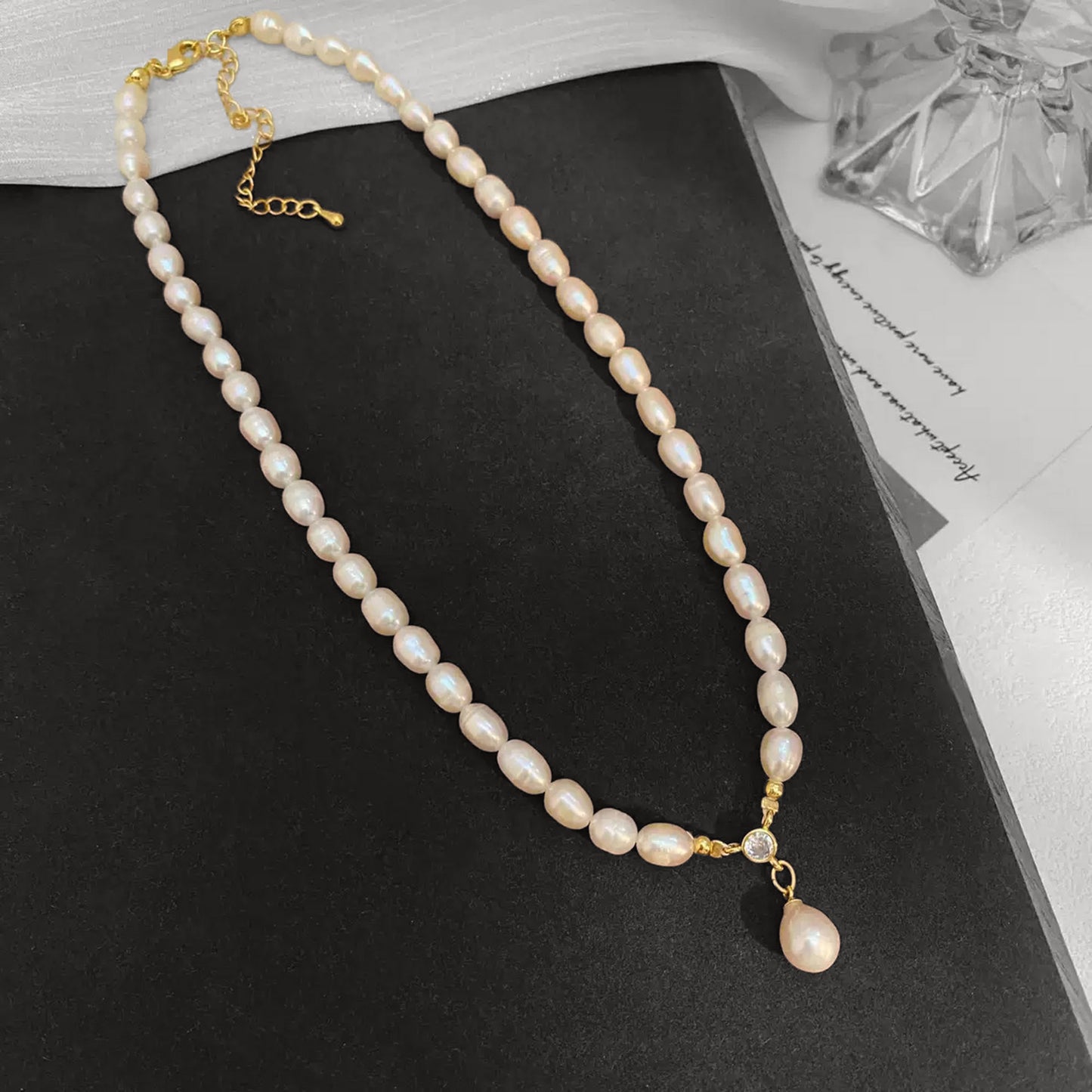 Pearl necklace with a gold chain on a black surface
