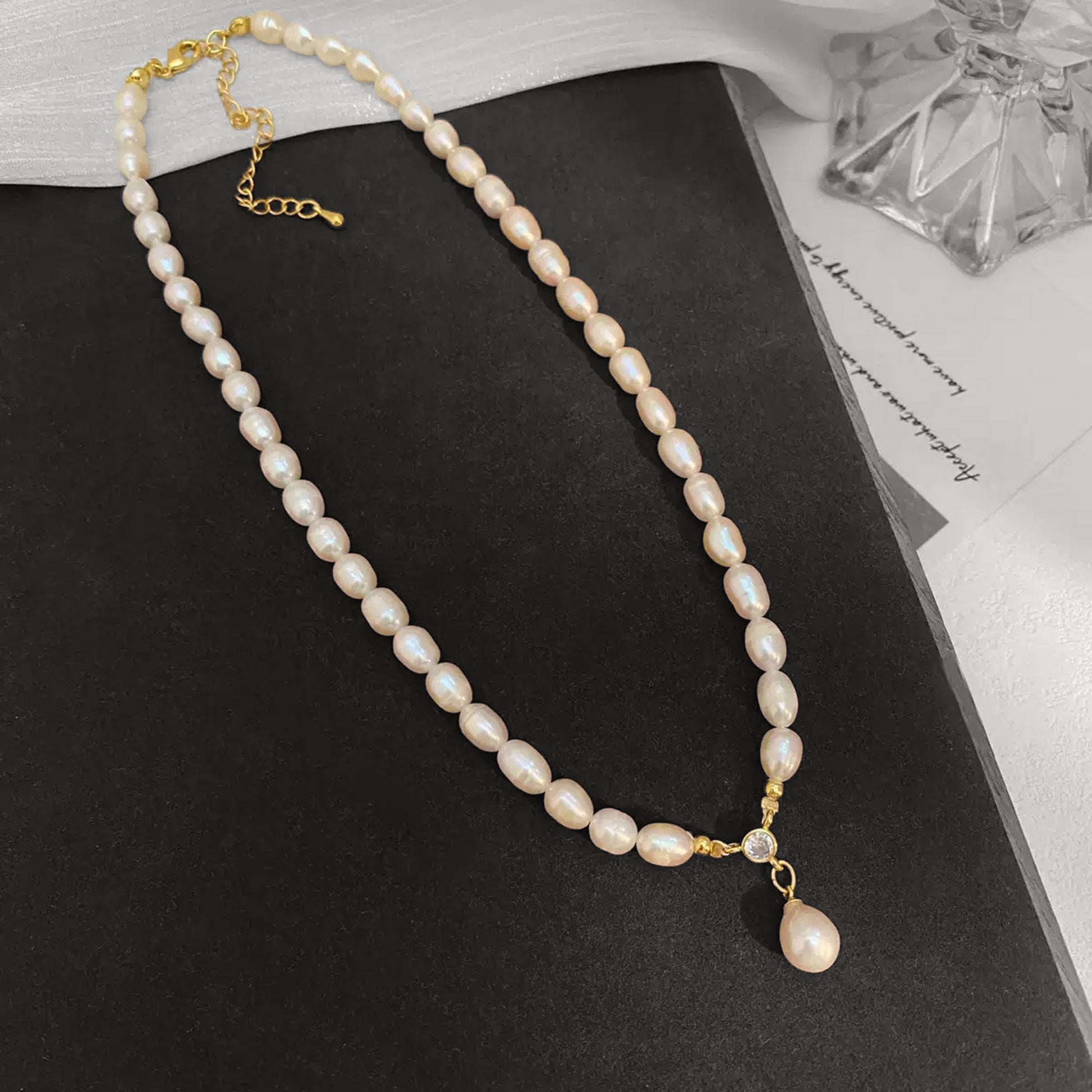 Pearl necklace with a gold chain on a black surface
