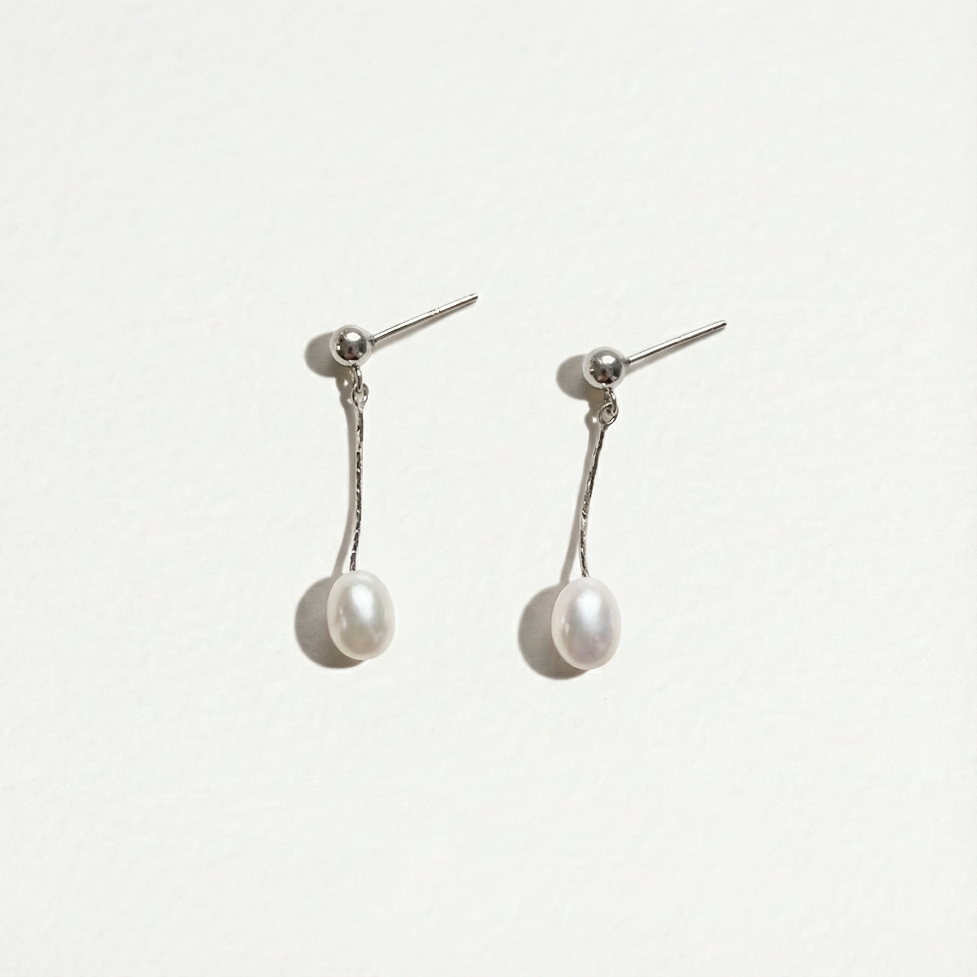 Front view of The Ethereal Drop pearl drop earrings in sterling silver with freshwater pearls on a light background