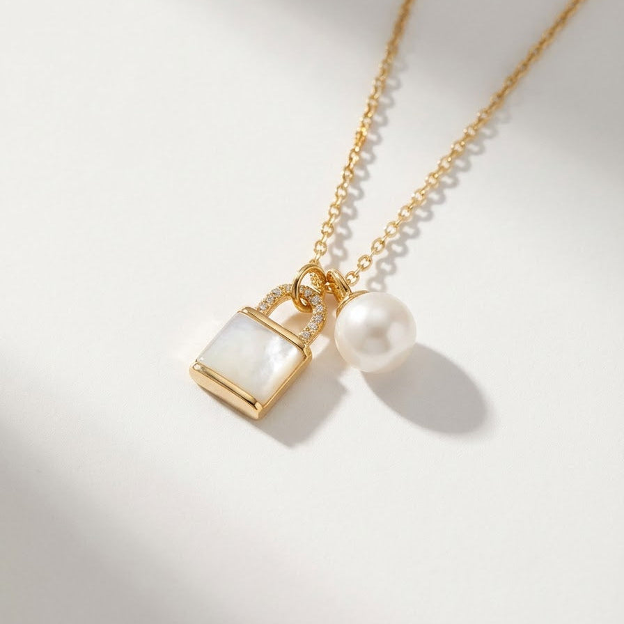 The Keeper’s Whisper necklace with a mother-of-pearl lock pendant and freshwater pearl shown on a light background