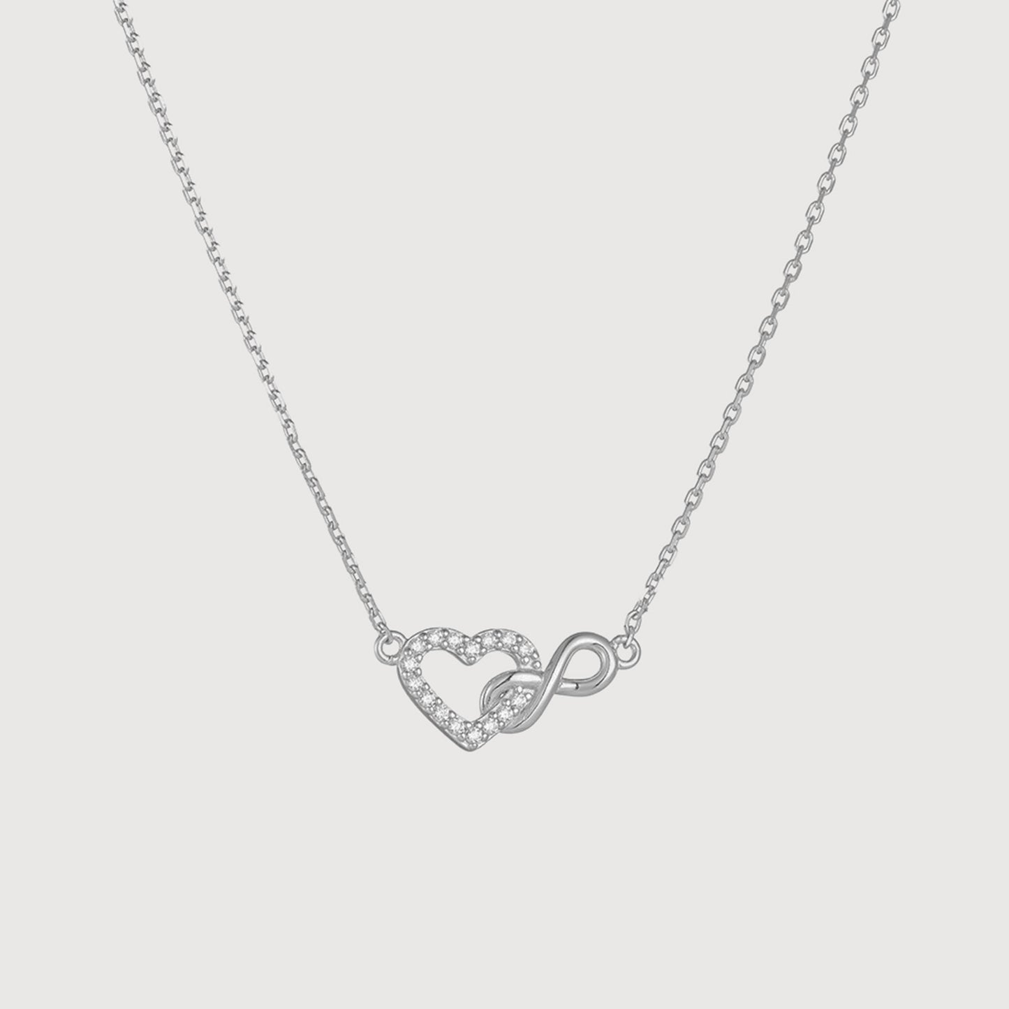 Silver necklace with a heart and infinity symbol pendant on a light gray background