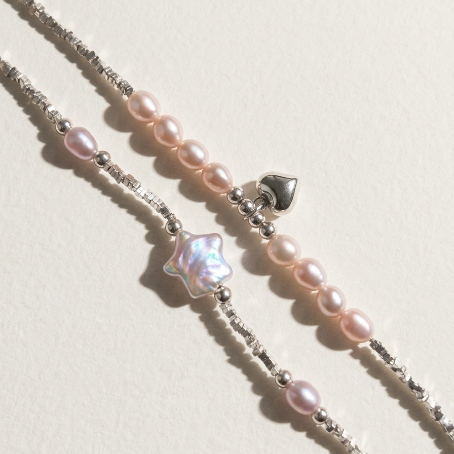 Close-up of two sterling silver bracelets styled together, including The Lavender Star bracelet and a heart charm bracelet