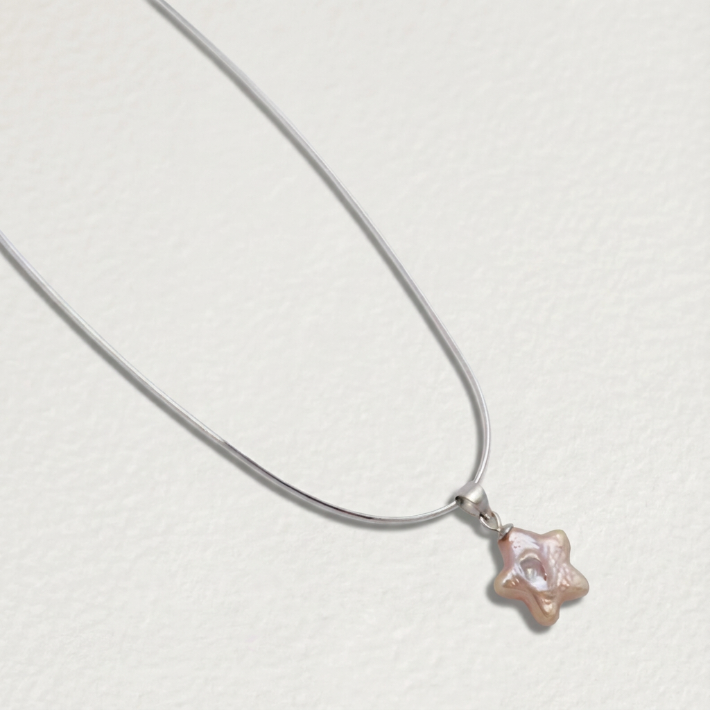 Pink star-shaped baroque pearl pendant necklace in sterling silver shown at an angle on a light beige background