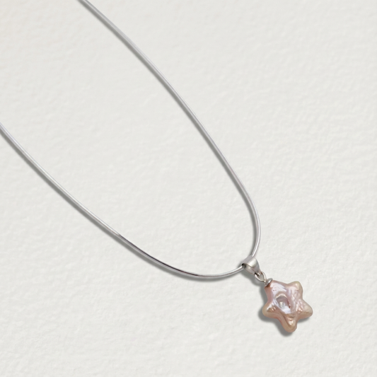 Pink star-shaped baroque pearl pendant necklace in sterling silver shown at an angle on a light beige background