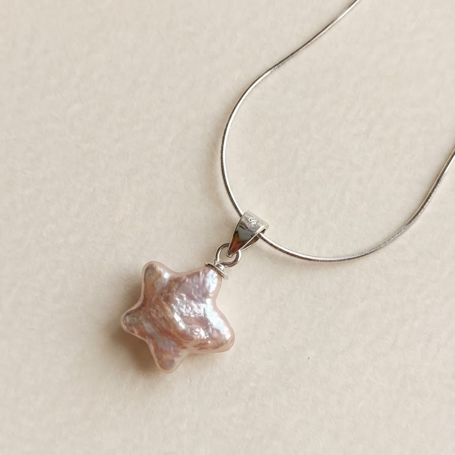 Close-up of a pink star-shaped baroque pearl pendant necklace in sterling silver on a light beige background