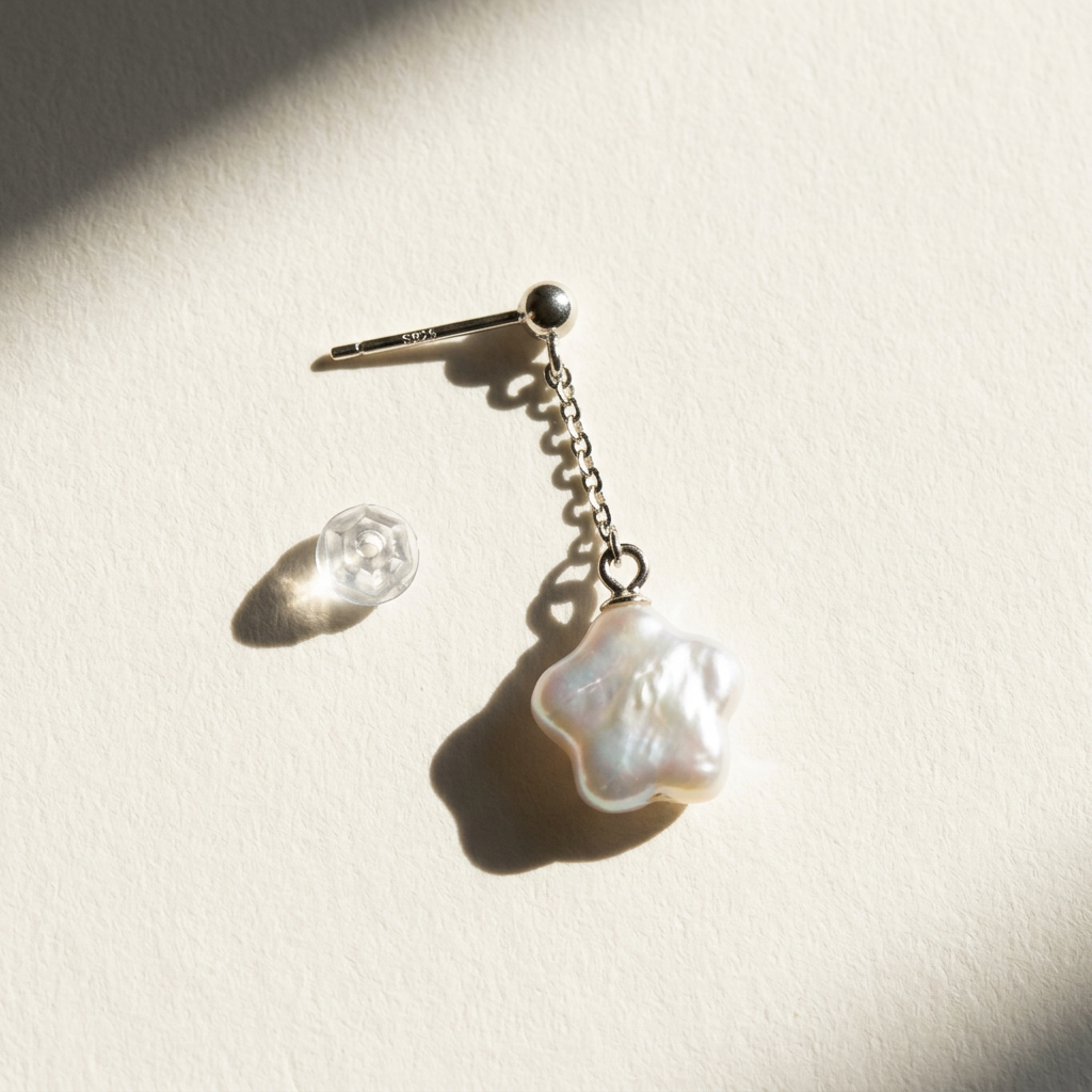 Close-up of a star baroque freshwater pearl drop earring in sterling silver with a clear push back on a light beige background