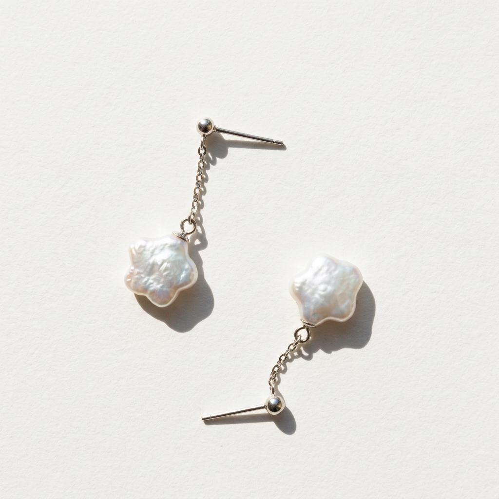 Close-up of star baroque freshwater pearl drop earrings in sterling silver on a light beige background