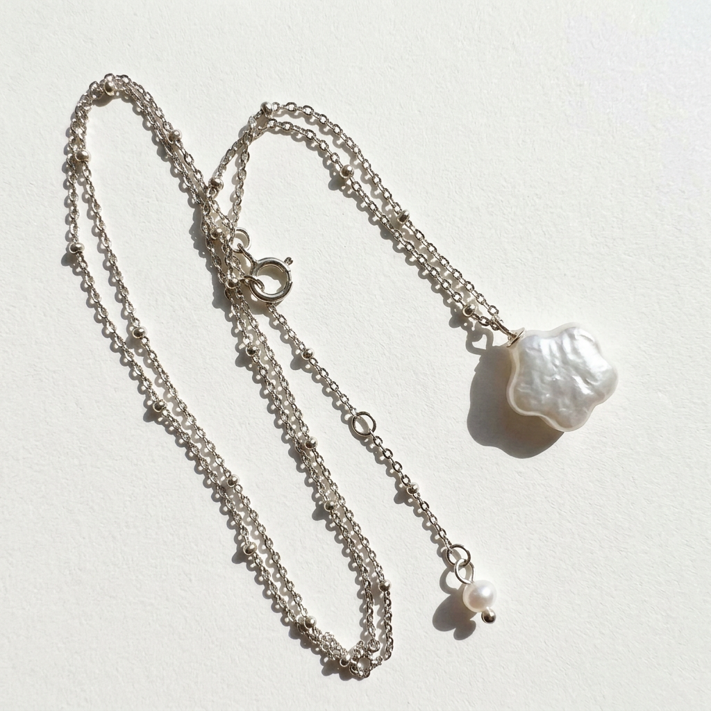 Angled detail of the star baroque freshwater pearl necklace in sterling silver showing the pendant, chain, clasp, and extension pearl