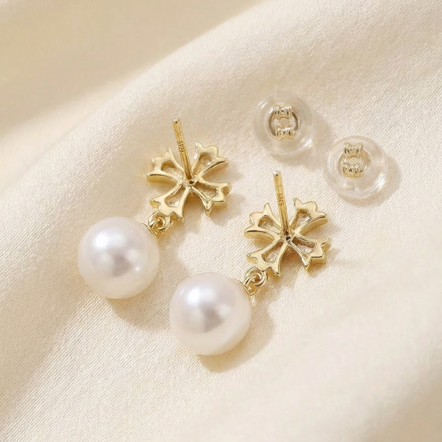 The Crosslight pearl drop earrings in 18K gold-plated sterling silver shown from the back with imitation pearl drops and butterfly backs on a warm beige fabric background