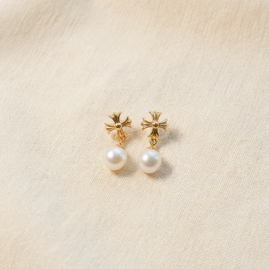 The Crosslight pearl drop earrings in 18K gold-plated sterling silver with imitation pearl drops on a warm beige fabric background