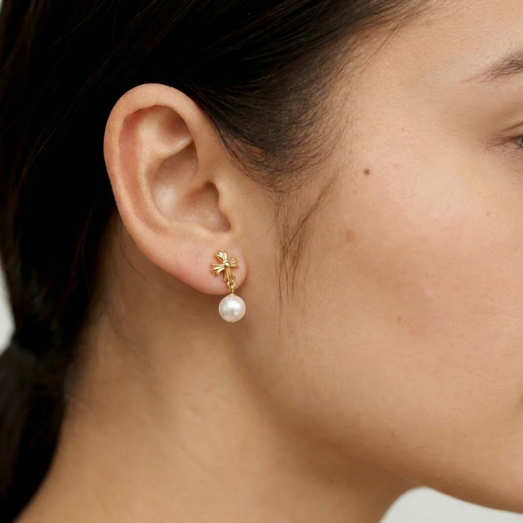 The Crosslight pearl drop earring worn on the ear in 18K gold-plated sterling silver with an imitation pearl drop