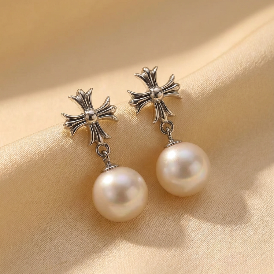 The Crosslight pearl drop earrings in sterling silver with imitation pearl drops shown in close-up on a warm beige fabric background