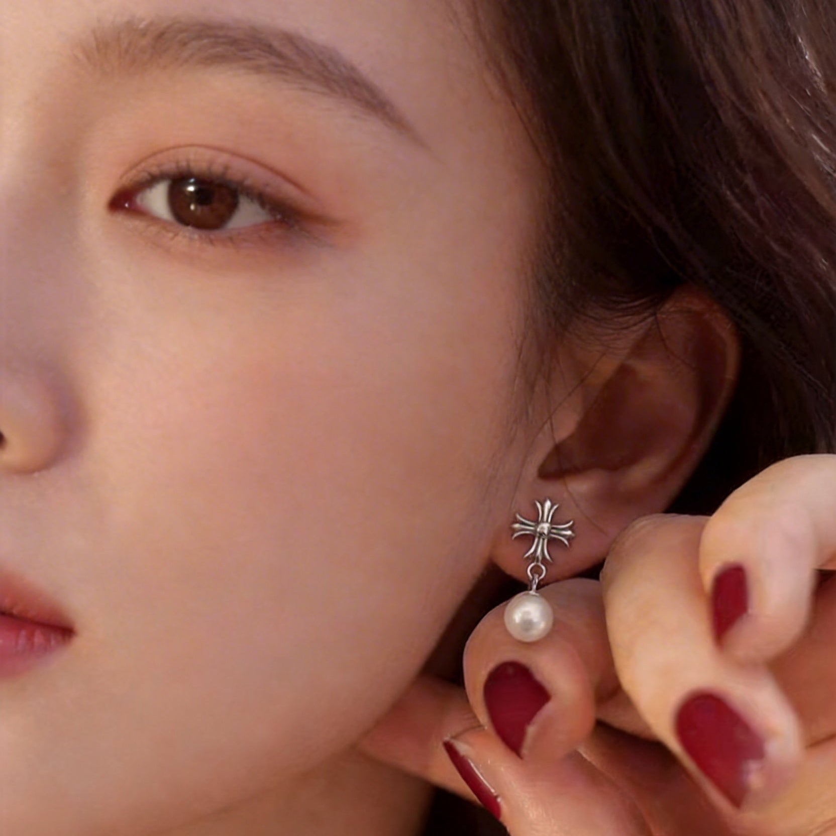 The Crosslight pearl drop earring worn on the ear in sterling silver with an imitation pearl drop, shown in close-up
