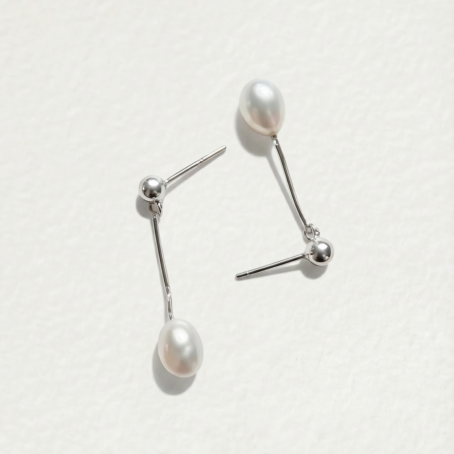 Flat lay detail of The Ethereal Drop pearl drop earrings in sterling silver with freshwater pearls on a light background