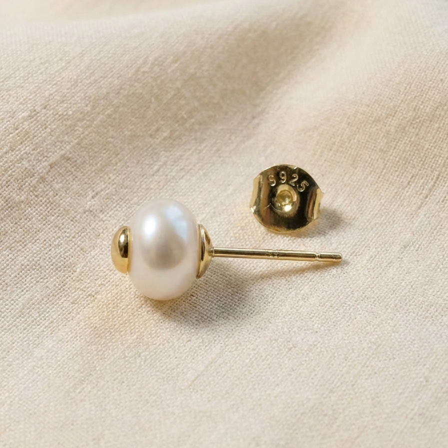 The Golden Heart pearl stud earring shown from the side with sterling silver post and S925 butterfly back on a warm beige fabric background