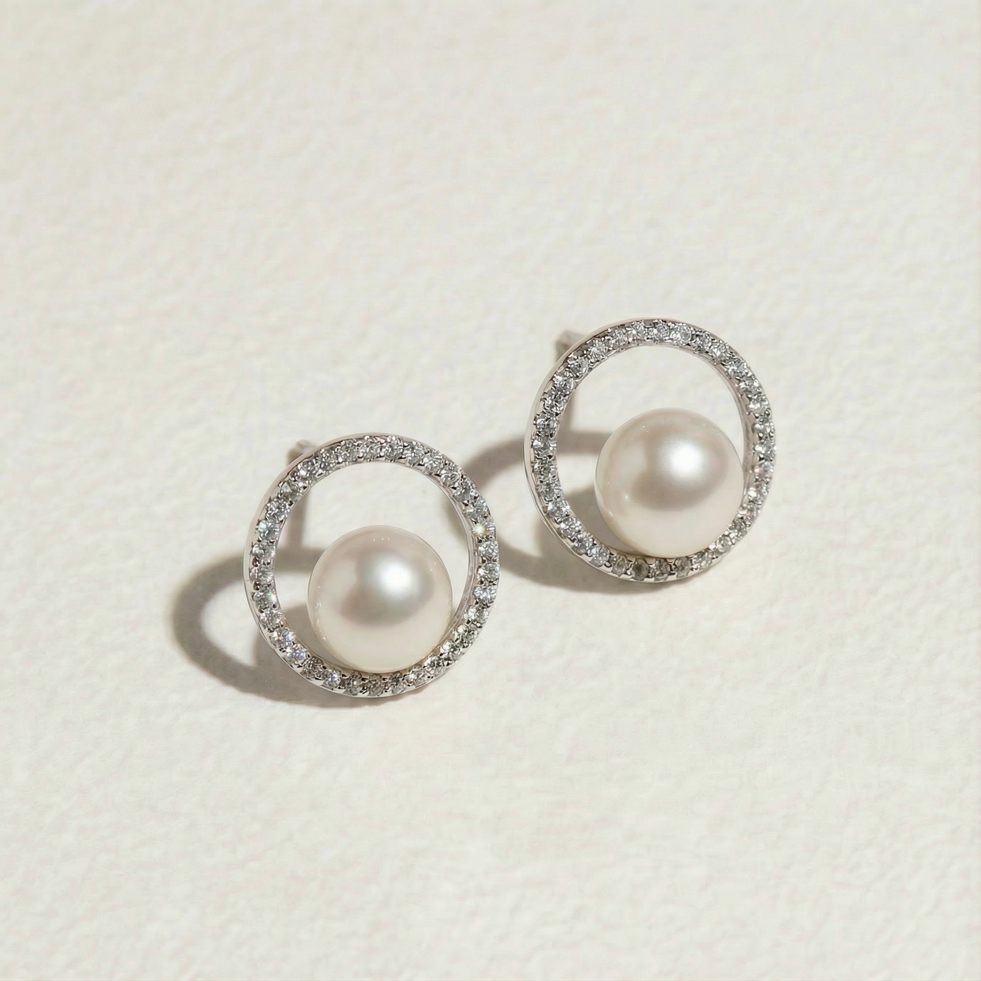 The Halo Pearl stud earrings with centred freshwater pearls and zircon-set circular halos shown on a light background