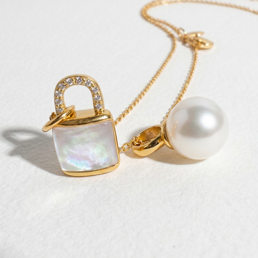 Close-up of The Keeper’s Whisper necklace featuring a mother-of-pearl lock pendant and a freshwater pearl on a light background