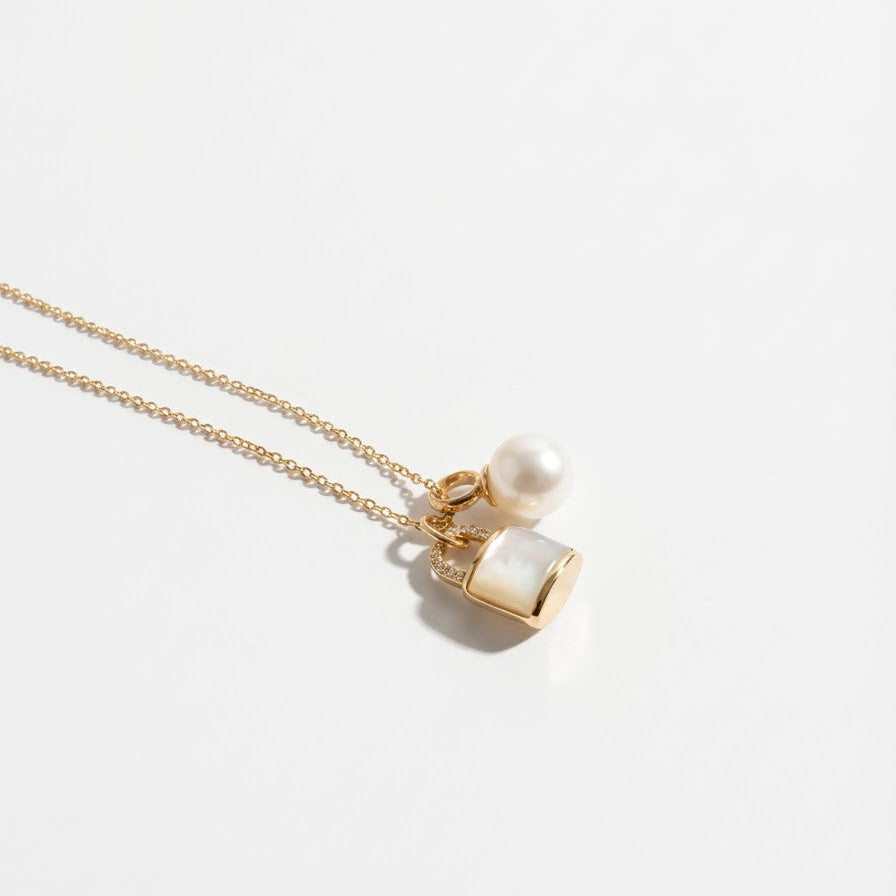 The Keeper’s Whisper necklace with a mother-of-pearl lock pendant and freshwater pearl arranged on a light background