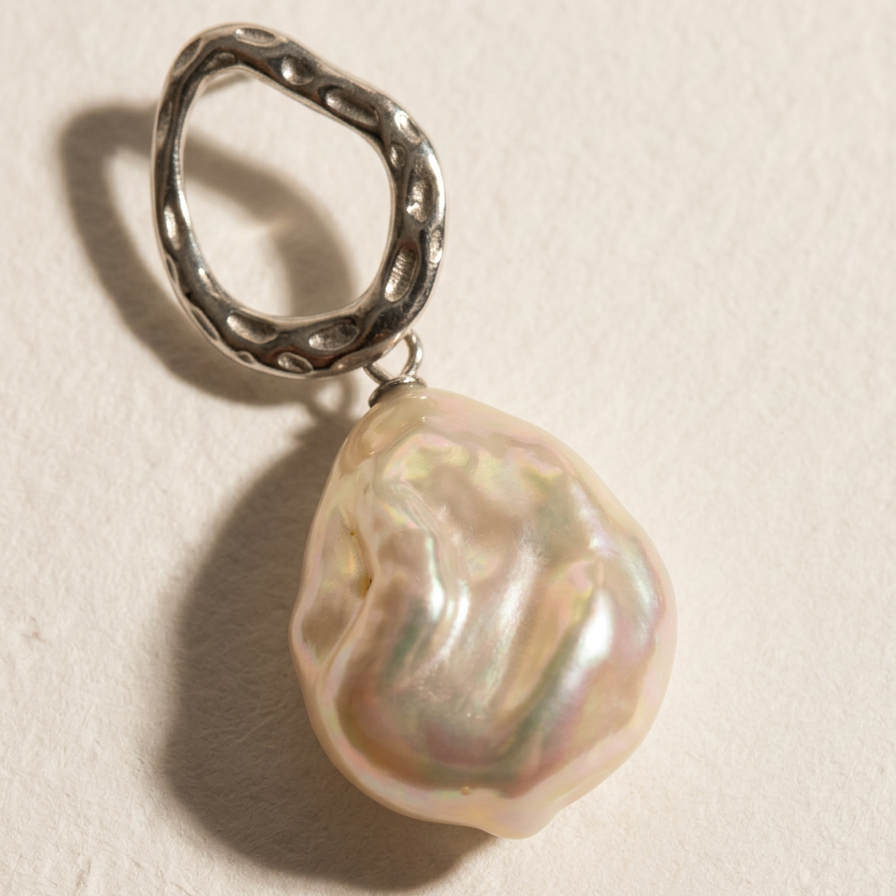 Close-up of a single The Silver Drift baroque pearl drop earring in sterling silver with a natural baroque freshwater pearl