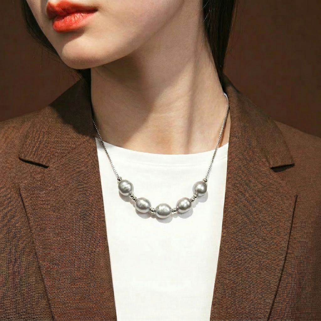 The Silver Mist grey baroque pearl necklace worn on the neck with a brown blazer and white top