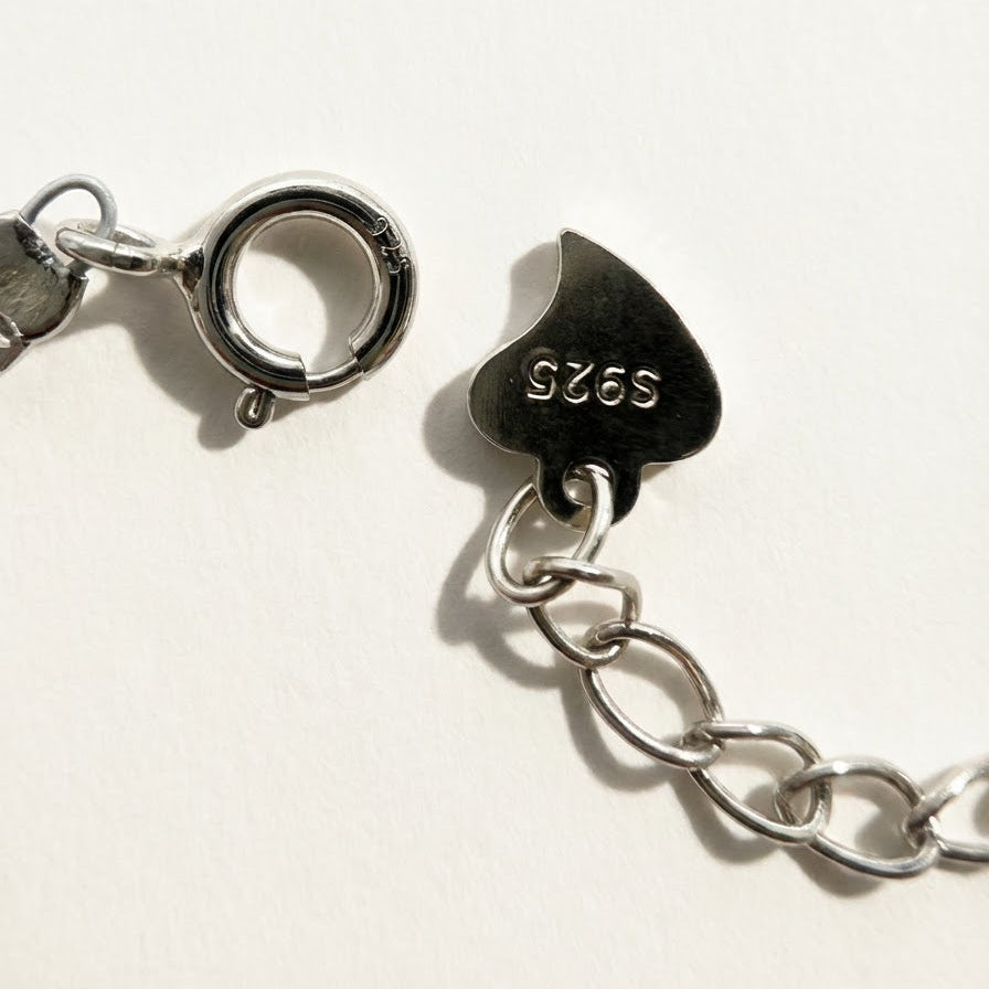 Close-up of The Soft Heart bracelet clasp, extension chain, and S925 heart tag on a light beige background