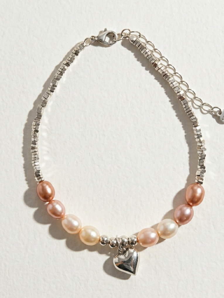 The Soft Heart freshwater pearl bracelet with peach-toned pearls and a sterling silver heart charm on a light beige background