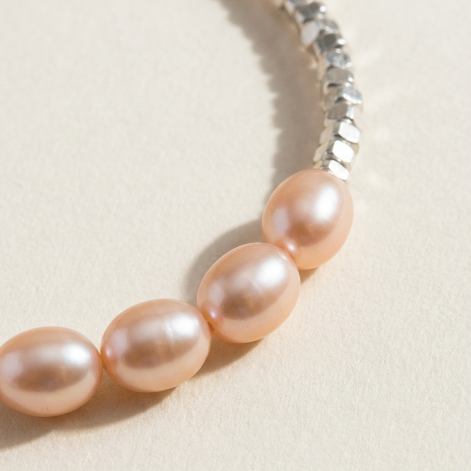 Close-up of The Soft Heart bracelet showing peach freshwater pearls and sterling silver details on a light beige background