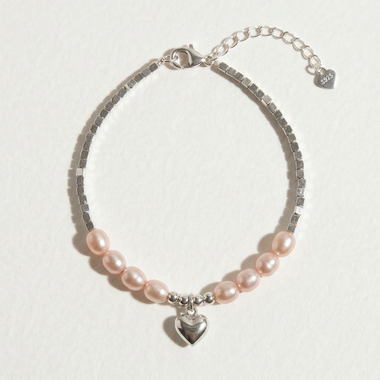 The Soft Heart freshwater pearl bracelet with peach-toned pearls, sterling silver beads, and a heart charm on a light beige background