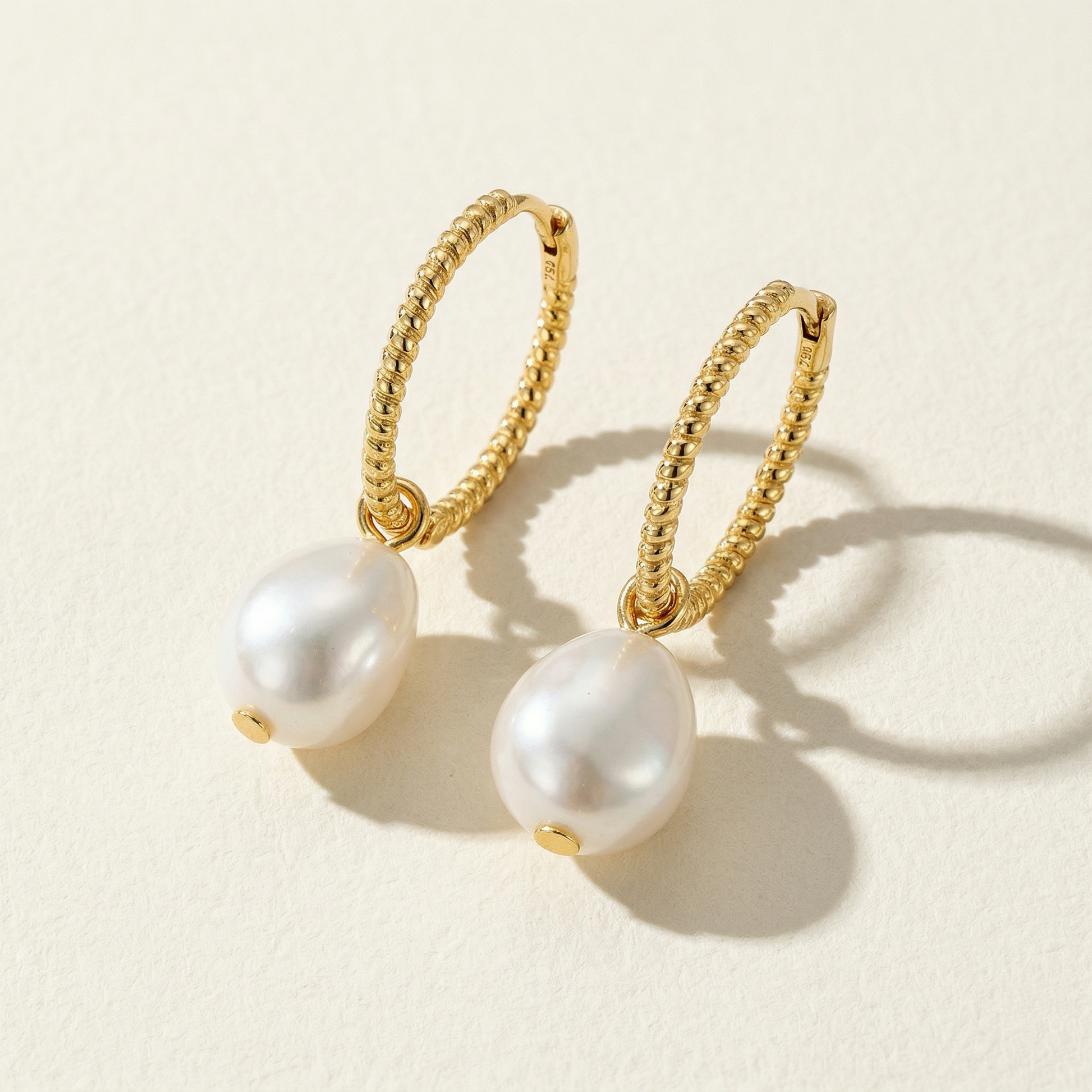 The Soft Hoop freshwater pearl huggie earrings in gold-plated sterling silver with pearl drops on a warm beige background