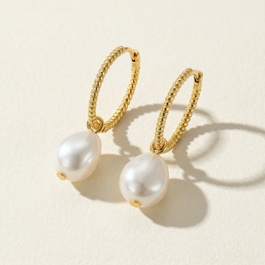 The Soft Hoop freshwater pearl huggie earrings in gold-plated sterling silver with pearl drops on a warm beige background