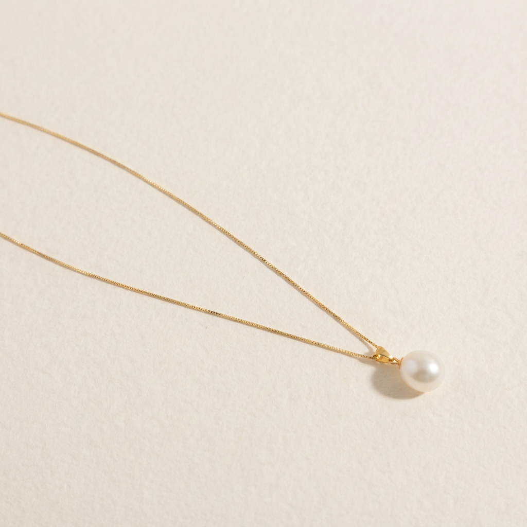 The Steady Pearl necklace in gold-plated sterling silver with a single baroque freshwater pearl on a warm beige background