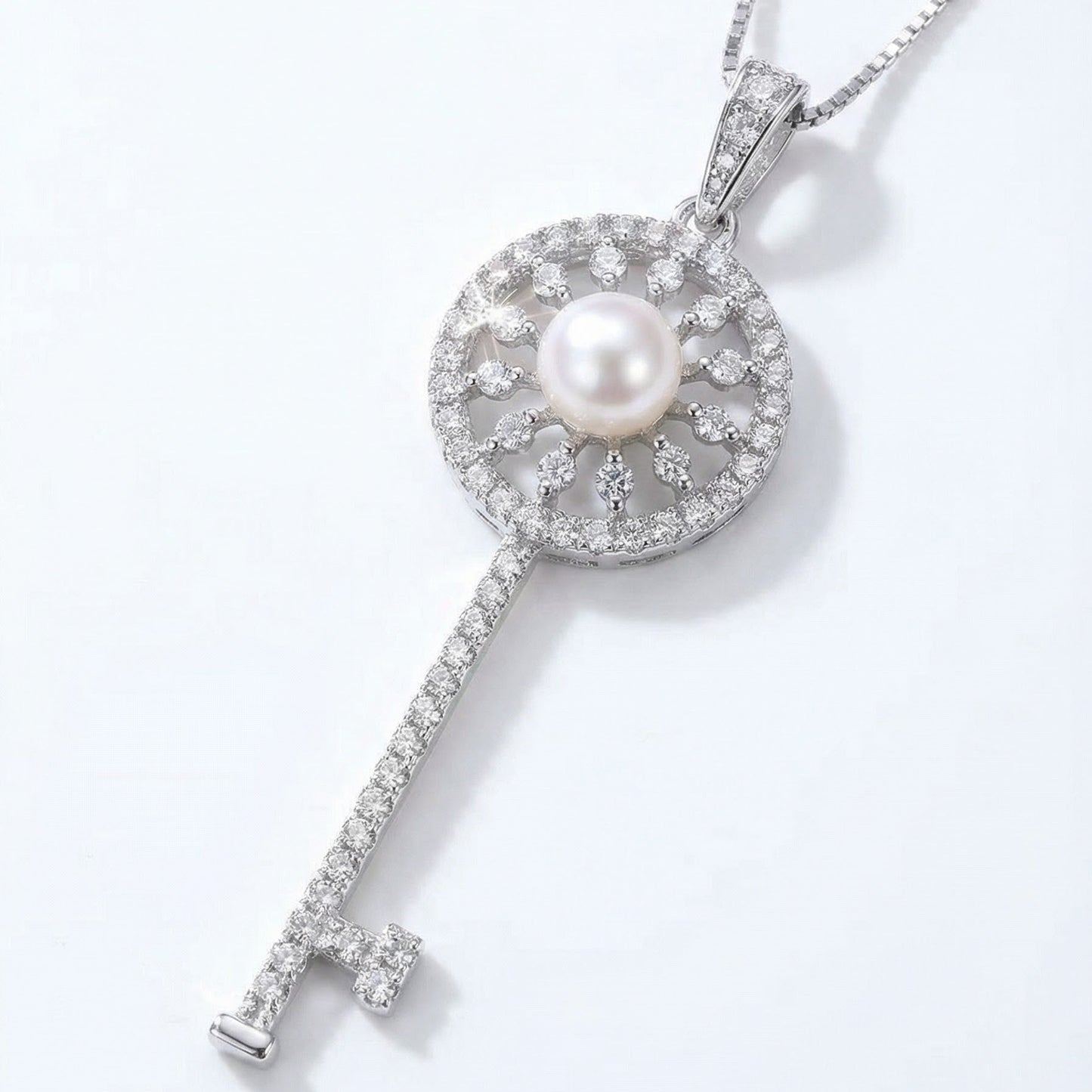 The Sunlit Key necklace in sterling silver with a freshwater pearl at the centre of a sunburst key pendant on a light grey background