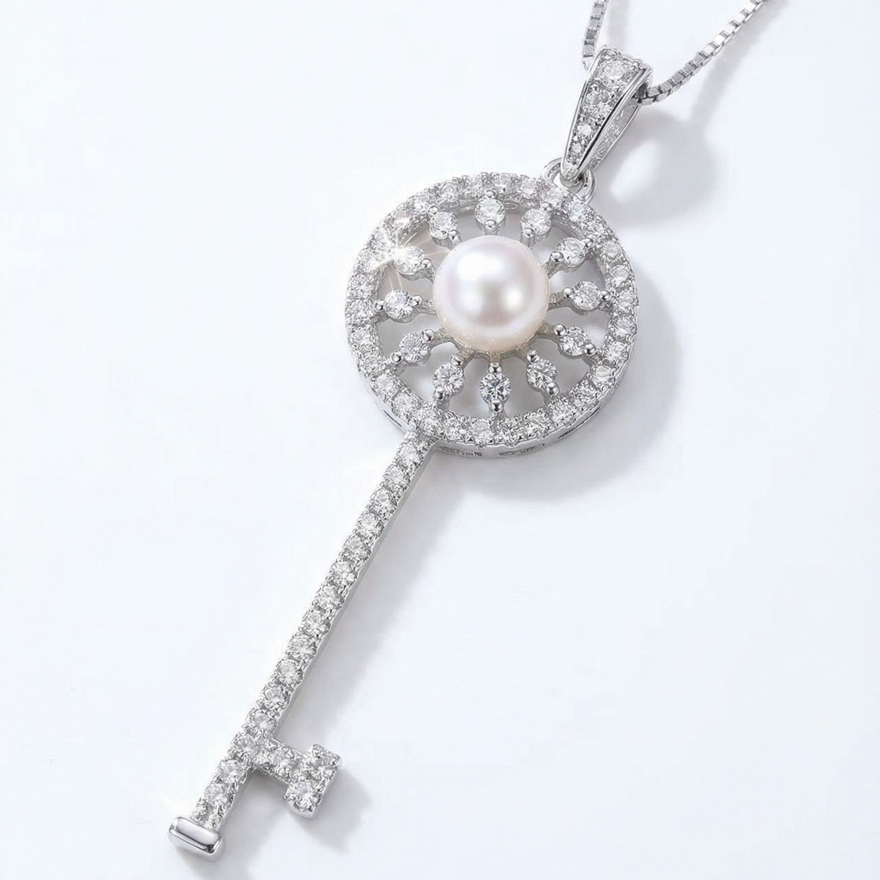 The Sunlit Key necklace in sterling silver with a freshwater pearl at the centre of a sunburst key pendant on a light grey background