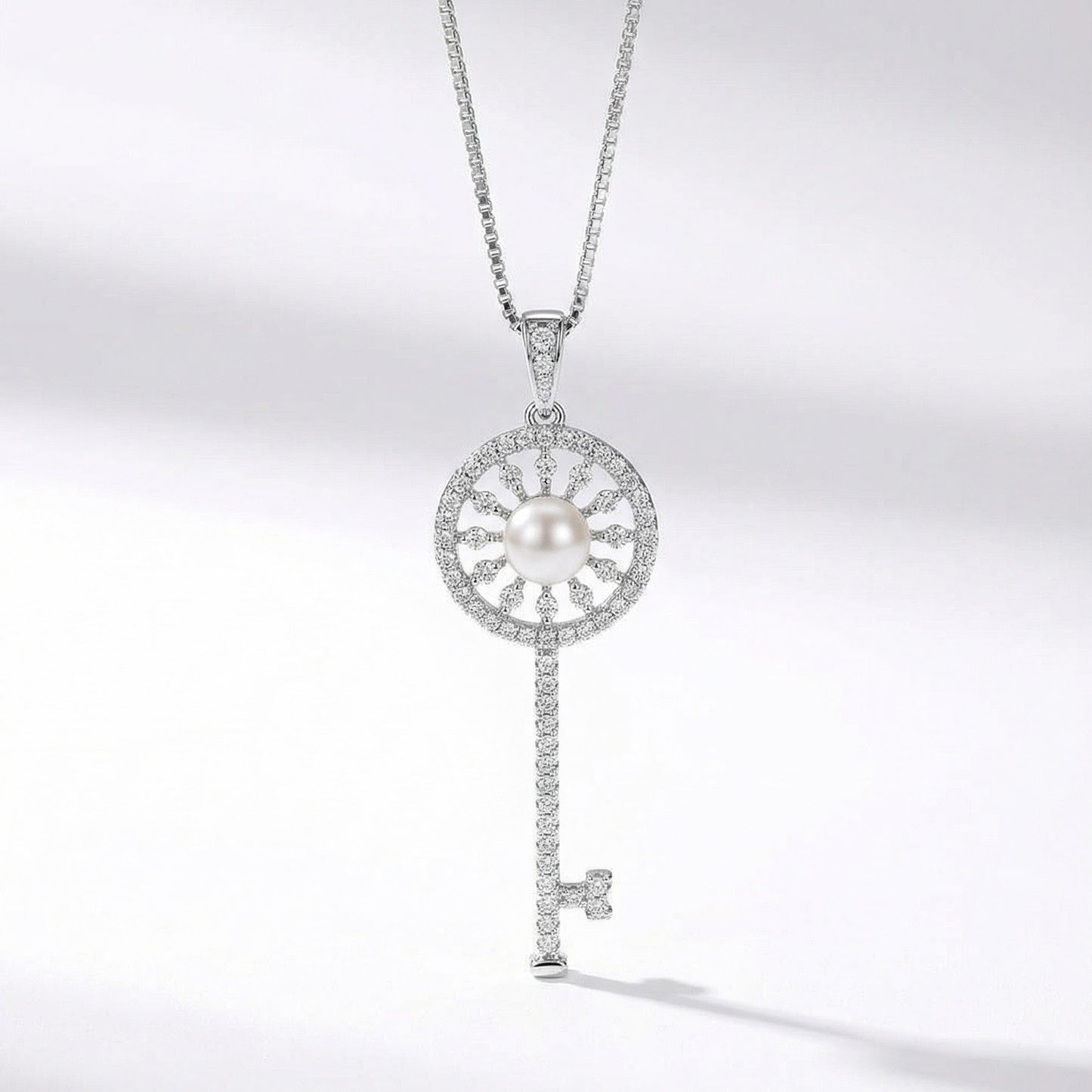 The Sunlit Key necklace in sterling silver with a freshwater pearl at the centre of a sunburst key pendant on a light grey background