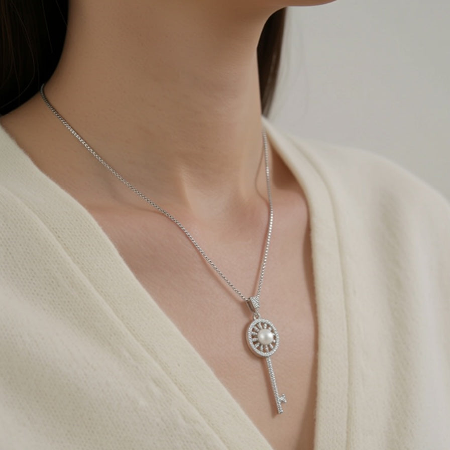 The Sunlit Key necklace worn at the chest in sterling silver with a freshwater pearl at the centre of a sunburst key pendant
