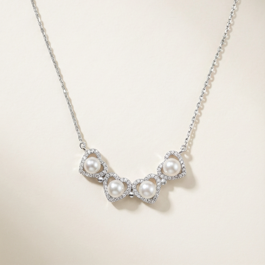 The Turning Heart necklace in sterling silver with four freshwater pearls framed by pavé zirconia on a warm beige background